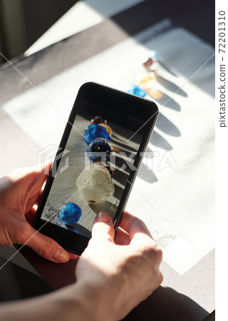Hands of young female with smartphone taking photo of row of large glass beads Hands of young female with smartphone taking photo of row of large glass beads 72201310