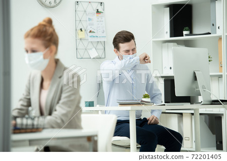 Male office manager in protective mask putting his face on arm while sneezing Male office manager in protective mask putting his face on arm while sneezing 72201405