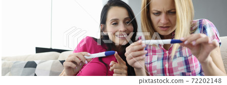 Two women are sitting on couch and looking at pregnancy tes 72202148