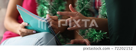 Two people are sitting on sofa with New Year's garland and making a list in diary. Two people are sitting on sofa with New Year's garland and making a list in diary. 72202152