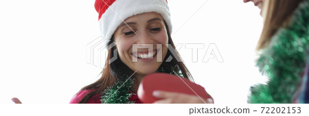 Smiling woman in santa claus hat looks at gift box Smiling woman in santa claus hat looks at gift box 72202153
