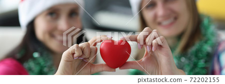 Two smiling woman in santa hats hold heart. Two smiling woman in santa hats hold heart. 72202155