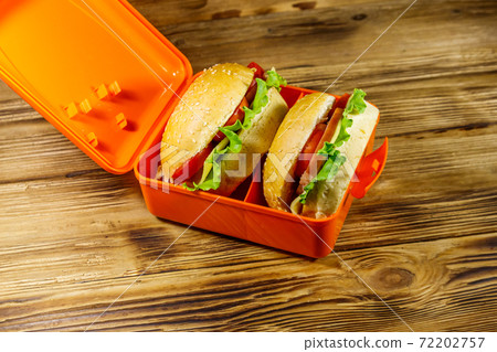 Lunch box with two homemade cheeseburgers on wooden table 72202757