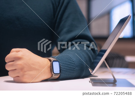 Businessman with digital tablet with white screen on the table and smart watch on his hand. A male freelancer works in a cafe. Businessman with digital tablet with white screen on the table and smart watch on his hand. A male freelancer works in a cafe. 72205488