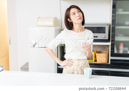 Think of a woman watching a smartphone in the kitchen Think of a woman watching a smartphone in the kitchen 72208644