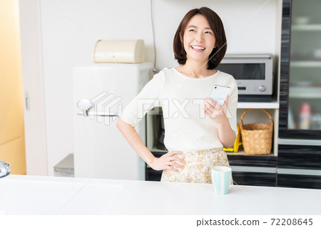 A woman watching a smartphone in the kitchen A woman watching a smartphone in the kitchen 72208645