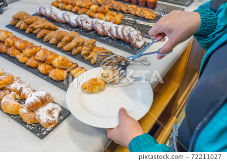 Woman selecting butter croissant at pastry counter in buffet restaurant 72211027