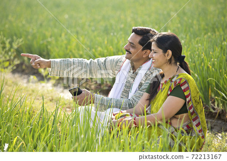 Happy Indian couple farmers examining crop in agricultural field 72213167