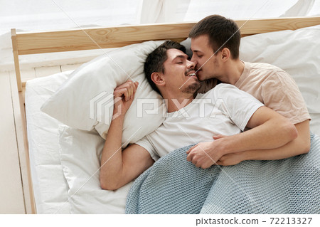 Happy gay couple lying on bed at home Happy gay couple lying on bed at home 72213327
