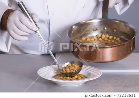 view of chickpea stew being served by a male chef using a ladle on an out of focus background view of chickpea stew being served by a male chef using a ladle on an out of focus background 72218631