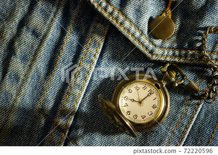 Vintage pocket watch is placed over an old blue denim shirt and the morning sun shines down in the top right corner. The concept of time importance. Closeup and copy space for text or your article. Vintage pocket watch is placed over an old blue denim shirt and the morning sun shines down in the top right corner. The concept of time importance. Closeup and copy space for text or your article. 72220596