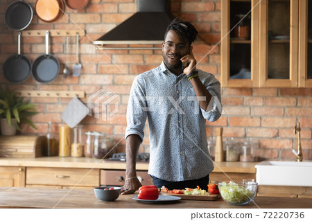 Smiling young mixed race man answering phone call, preparing food. Smiling young mixed race man answering phone call, preparing food. 72220736