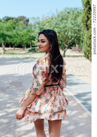 Beautiful brunette woman in a dress with flowers walks in the park in spring 72220997
