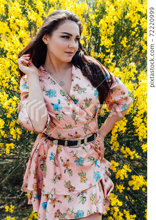 Beautiful brunette woman in a dress with flowers walks in the park in spring Beautiful brunette woman in a dress with flowers walks in the park in spring 72220999