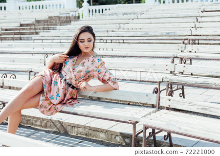 Beautiful brunette woman in a dress with flowers walks in the park in spring Beautiful brunette woman in a dress with flowers walks in the park in spring 72221000