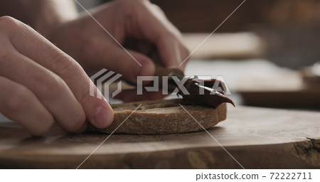 man spreading chocolate hazelnut spread on ciabatta slice on wood board man spreading chocolate hazelnut spread on ciabatta slice on wood board 72222711
