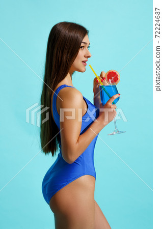 Woman in swimsuit poses with coctail, side view Woman in swimsuit poses with coctail, side view 72224687