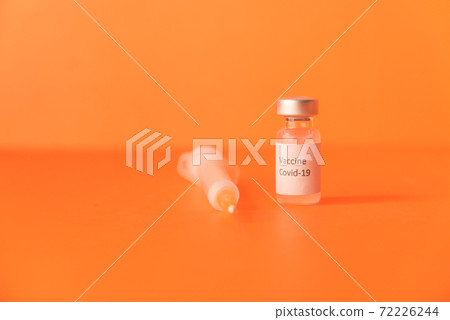 Close up of coronavirus vaccine and syringe on orange background 72226244