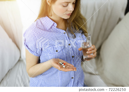 Close-up woman holding pills time to take medications, cure for headache. Medicine concept during self isolation and Coronavirus pandemic 72226250