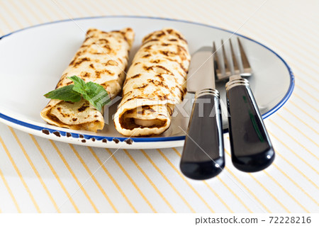 thin pancakes rolled crepes mint on a plate with knife and fork 72228216