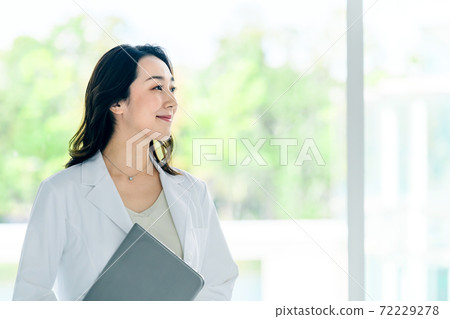 A female doctor with a smiling computer in a lab coat at the hospital A female doctor with a smiling computer in a lab coat at the hospital 72229278