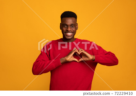 Kind black guy shaping hands like heart, making love gesture near chest 72229410