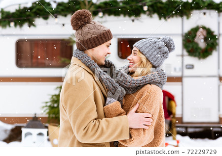 Warming Love. Happy Young Couple Cuddling Under Falling Snow, Covering With Scarf Warming Love. Happy Young Couple Cuddling Under Falling Snow, Covering With Scarf 72229729