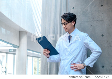 A male doctor with a smiling clipboard in a lab coat at the hospital 72231476