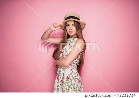 Winsome girl in romantic dress with flower print and straw hat posing smiling pretty on a purple background Winsome girl in romantic dress with flower print and straw hat posing smiling pretty on a purple background 72231734