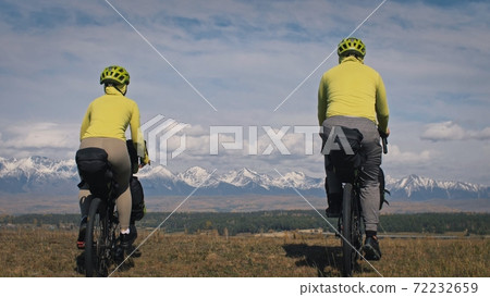 The man and woman travel on mixed terrain cycle touring with bikepacking. The two people journey with bicycle bags. Mountain snow capped. The man and woman travel on mixed terrain cycle touring with bikepacking. The two people journey with bicycle bags. Mountain snow capped. 72232659