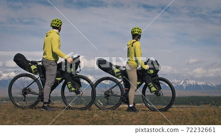 The man and woman travel on mixed terrain cycle touring with bikepacking. The two people journey with bicycle bags. Mountain snow capped. The man and woman travel on mixed terrain cycle touring with bikepacking. The two people journey with bicycle bags. Mountain snow capped. 72232661