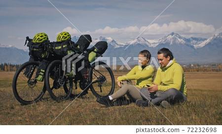 The man and woman travel on mixed terrain cycle touring with bikepacking. The two people journey with bicycle bags. Mountain snow capped. The man and woman travel on mixed terrain cycle touring with bikepacking. The two people journey with bicycle bags. Mountain snow capped. 72232698