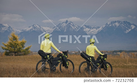 The man and woman travel on mixed terrain cycle touring with bikepacking. The two people journey with bicycle bags. Mountain snow capped. The man and woman travel on mixed terrain cycle touring with bikepacking. The two people journey with bicycle bags. Mountain snow capped. 72232708
