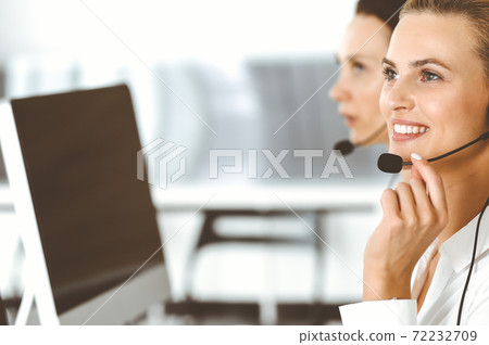 Blond female customer service representative and her colleague are consulting clients online using headset. Call center and business people concept Blond female customer service representative and her colleague are consulting clients online using headset. Call center and business people concept 72232709