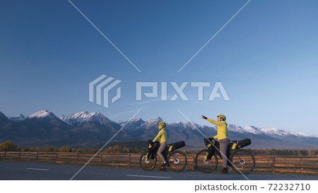 The man and woman travel on mixed terrain cycle touring with bikepacking. The couple journey with bicycle bags. Mountain snow capped. The man and woman travel on mixed terrain cycle touring with bikepacking. The couple journey with bicycle bags. Mountain snow capped. 72232710