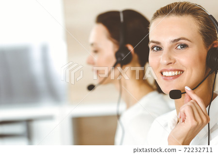 Blond female customer service representative and her colleague are consulting clients online using headset. Call center and business people concept Blond female customer service representative and her colleague are consulting clients online using headset. Call center and business people concept 72232711