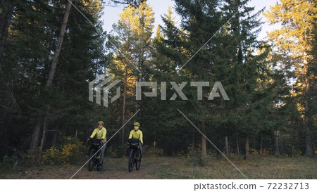 The man and woman travel on mixed terrain cycle touring with bikepacking. The couple journey with bicycle bags. Magic forest park. The man and woman travel on mixed terrain cycle touring with bikepacking. The couple journey with bicycle bags. Magic forest park. 72232713