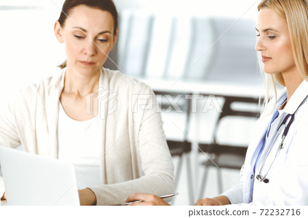 Woman-doctor sitting and communicating with her female patient in clinic. Blonde physician happy to help. Medicine concept Woman-doctor sitting and communicating with her female patient in clinic. Blonde physician happy to help. Medicine concept 72232716