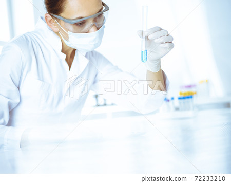 Female laboratory assistant analyzing test tube with blue liquid. Medicine, health care and researching concept 72233210