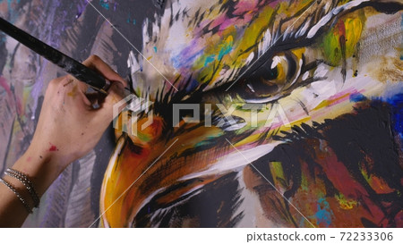 Artist designer draws an eagle on the wall. Craftsman decorator paints a picture with acrylic oil color brush. Close-up dark magic cinematic look. 72233306