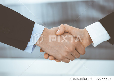 Businessman and woman shaking hands in office. Concept of handshake as success symbol in business Businessman and woman shaking hands in office. Concept of handshake as success symbol in business 72233308