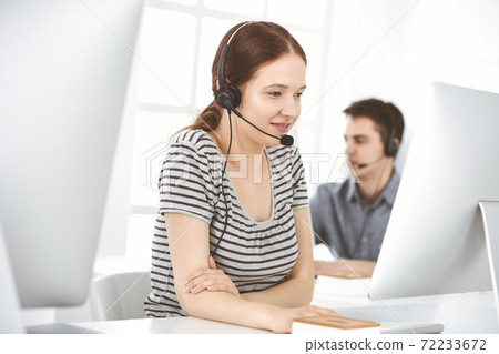 Casual dressed young woman using headset and computer while talking with customers online. Group of operators at work. Call center, business concept 72233672