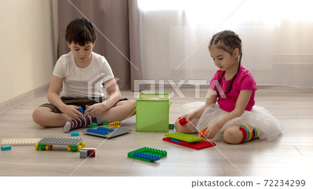 Two children, a boy and a girl, are sitting on the floor in the room, play in plastic construction 72234299