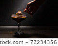 A woman's hand with a spoon takes jelly coffee with milk in a glass bowl, which is sprinkled with chocolate chips. Deep shadows. Rustic. 72234356