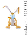 Cute soft toy hare with a flower and in a medical mask on a white background. Isolate. 72234381
