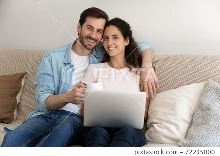 Portrait happy young couple sitting on couch with laptop Portrait happy young couple sitting on couch with laptop 72235000