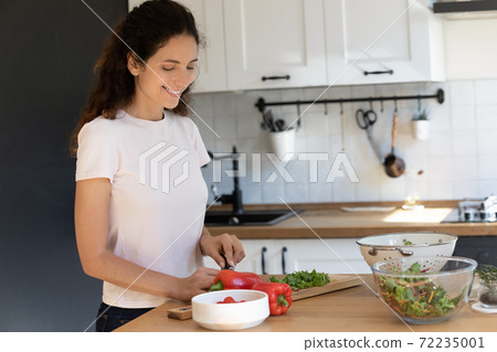 Smiling attractive woman cutting fresh vegetables in modern kitchen 72235001