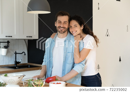 Portrait smiling man and woman hugging, standing in modern kitchen 72235002