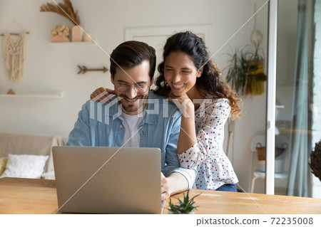 Happy young man and woman hugging, using laptop together 72235008