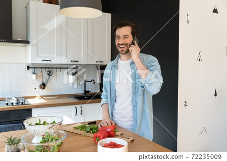 Overjoyed man talking on phone, standing in modern kitchen Overjoyed man talking on phone, standing in modern kitchen 72235009